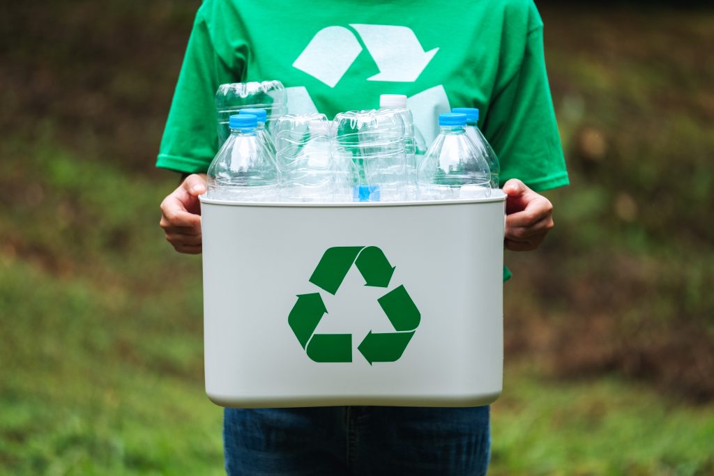 Person holding a recycle bin filled with plastic bottles, symbolizing collection stage in plastic recycling chain.