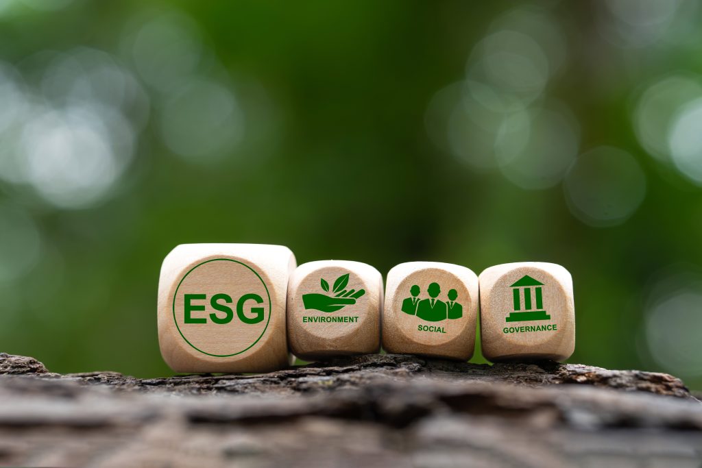 Wooden blocks with ESG, Environment, Social, and Governance icons placed on natural wood with a green forest background.